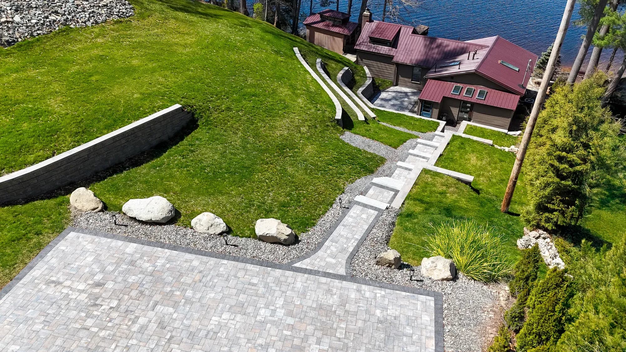 Upper paver driveway and boulder border at the head of the stairway toward the waterfront home.