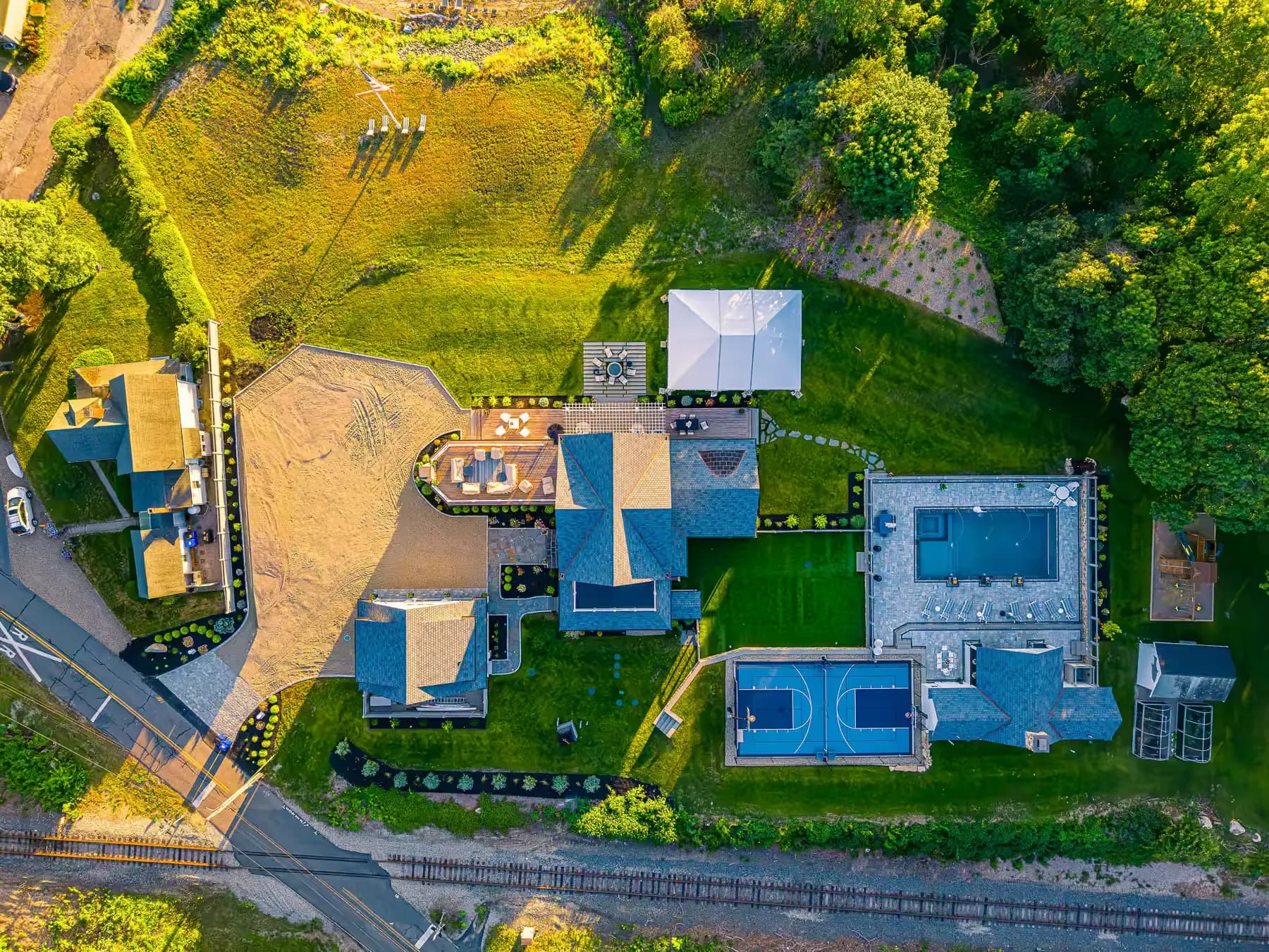 Aerial view of the property showing the pool terrace, sport court, lawn, and paved arrival area.