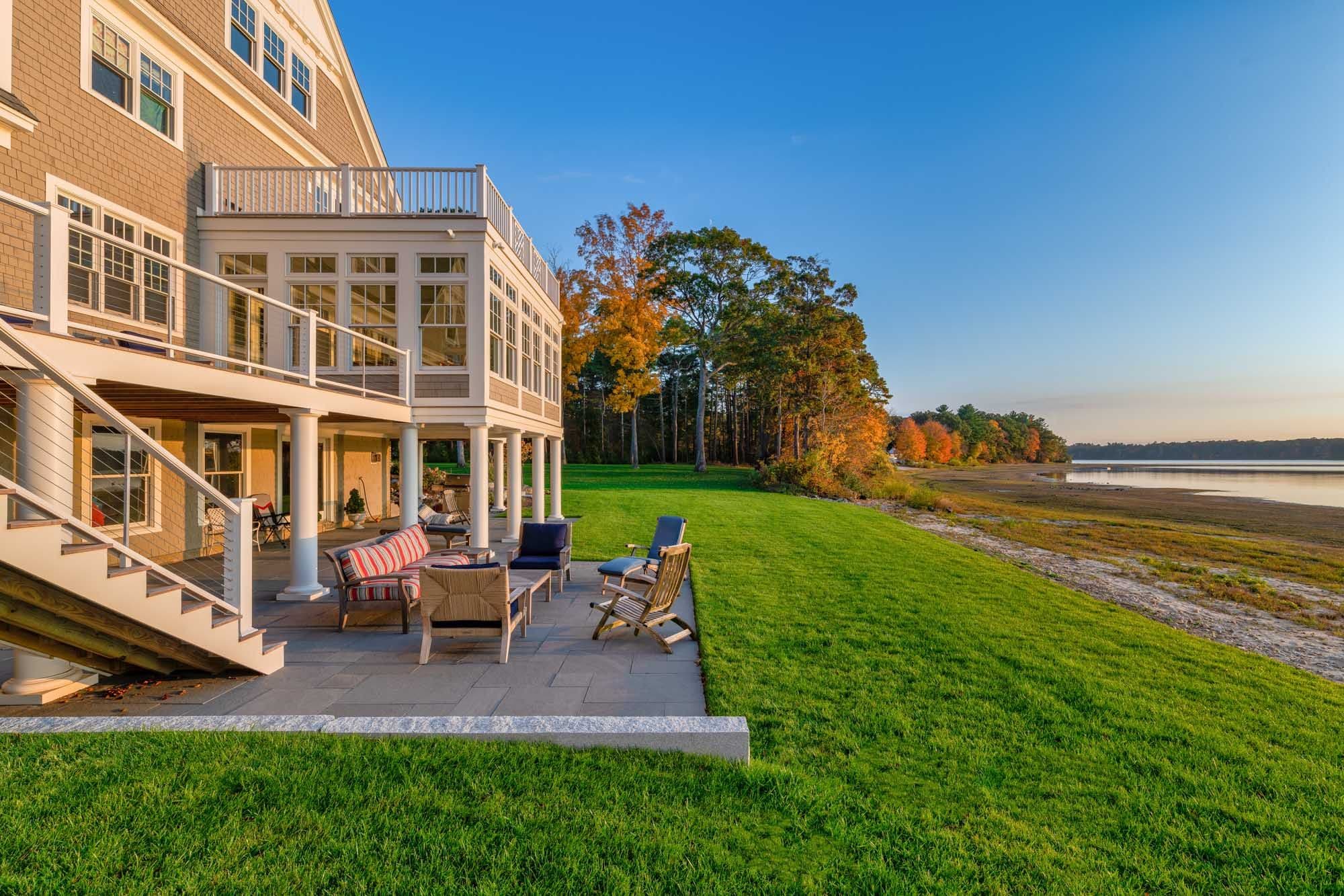 Bluestone patio and outdoor seating beneath the waterfront home, opening onto the lawn.