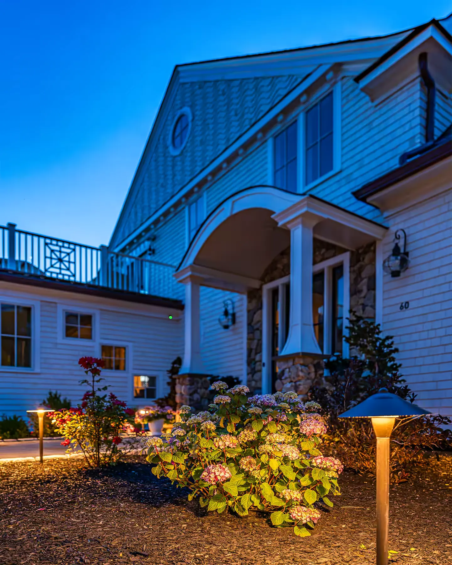 Path lighting highlights hydrangeas and a curved walkway beside the house.