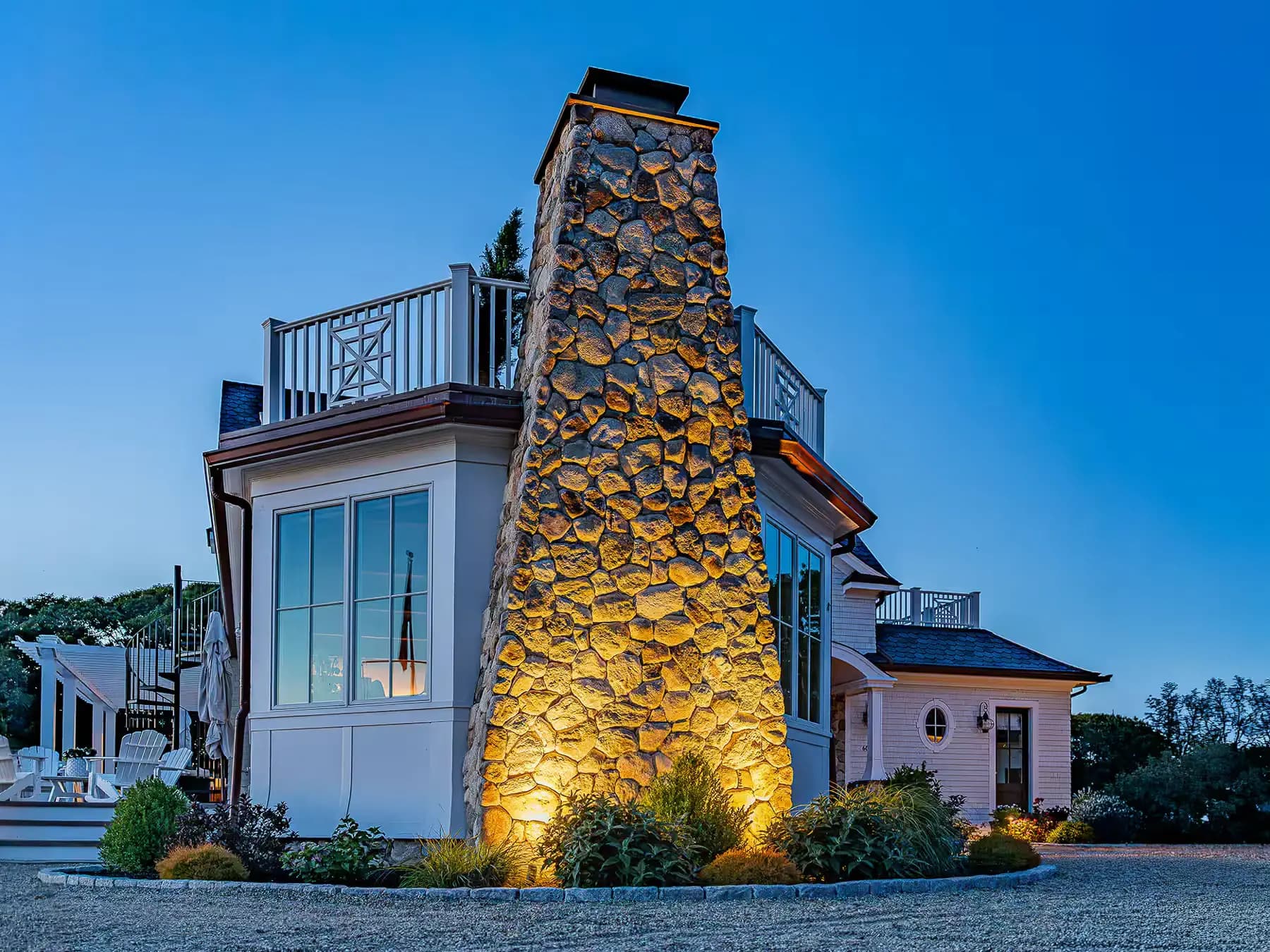 Landscape uplighting illuminates the stone chimney and planting beds at dusk.