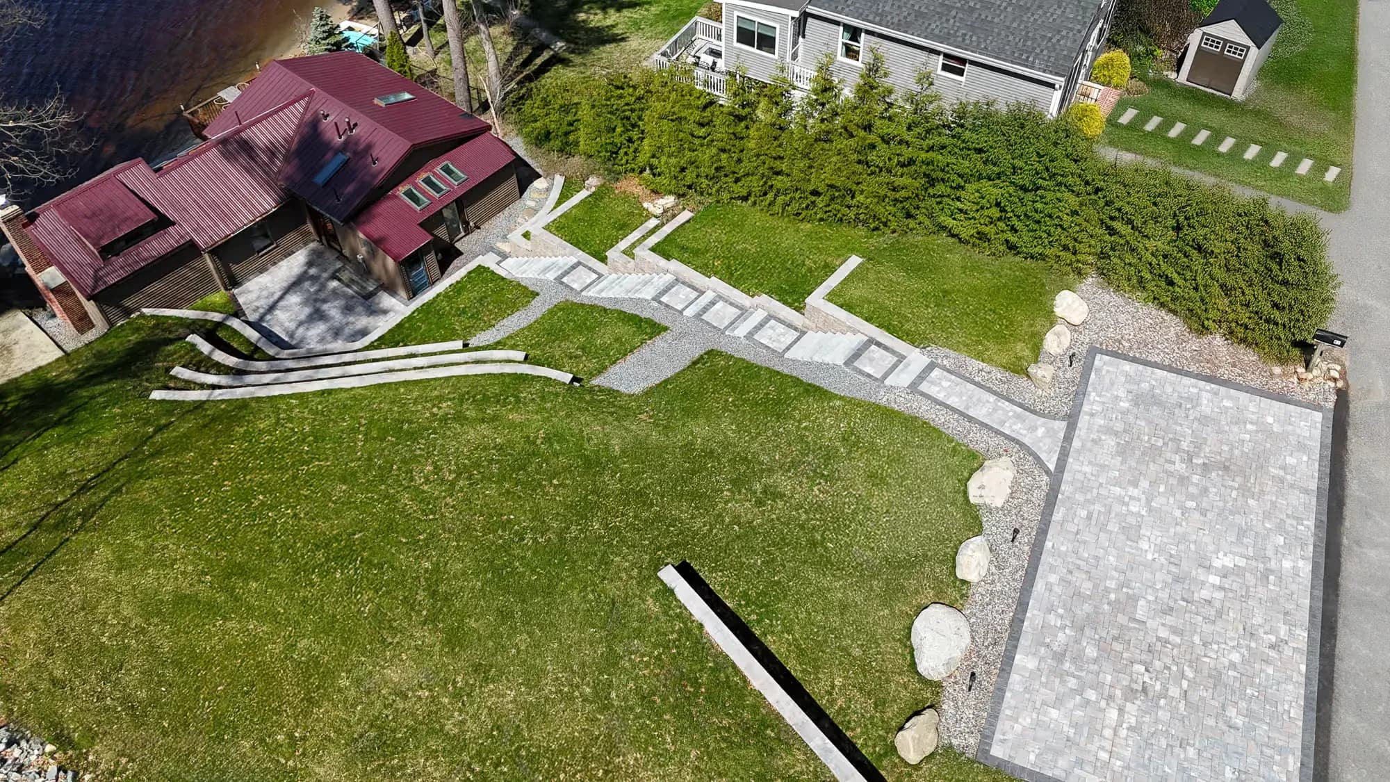 Aerial view connecting the upper driveway, hillside steps, lower patio, and waterfront home.