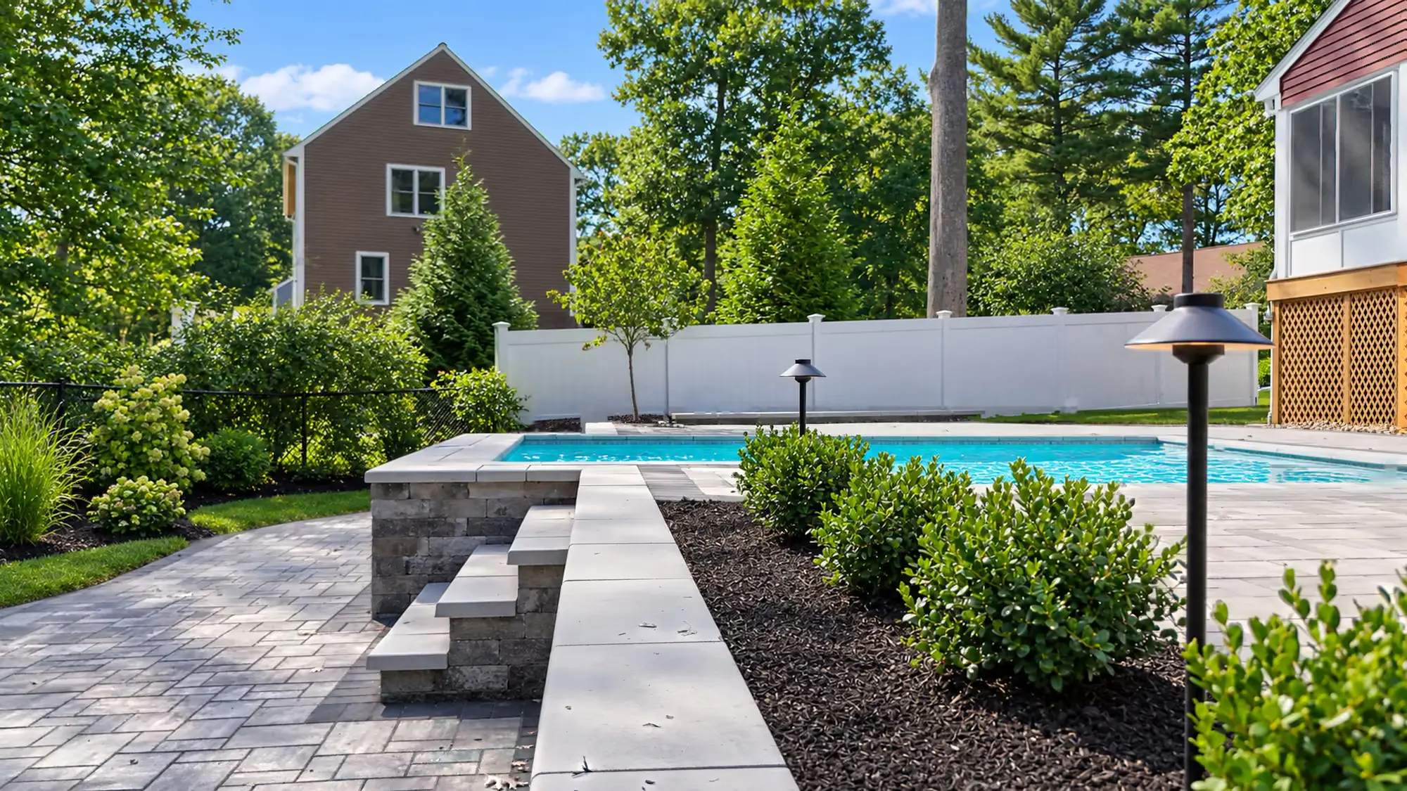 Steps and a capped retaining wall leading up to the pool, with path lights in the planting bed.