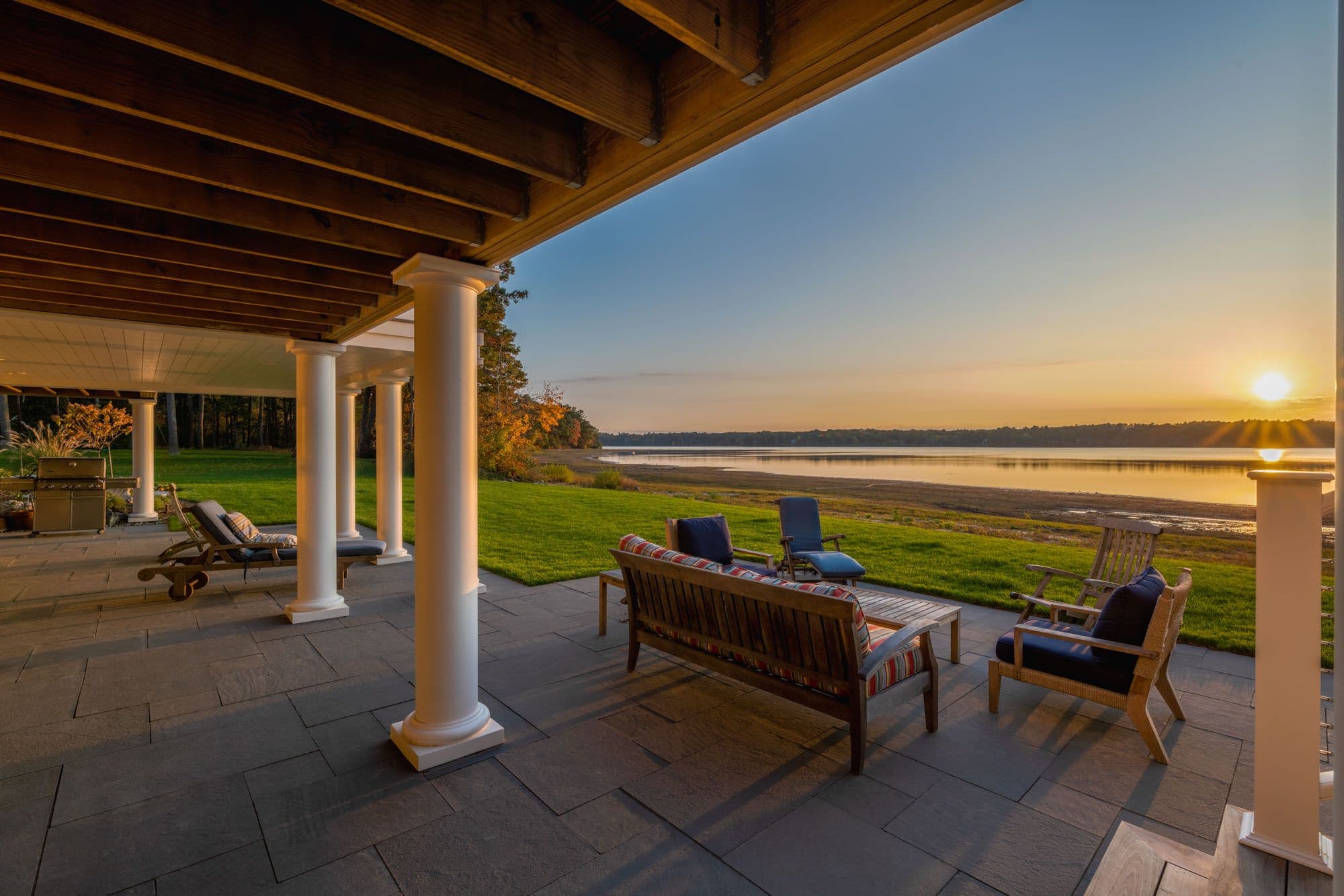 Covered bluestone terrace with conversation seating facing the water at sunset.