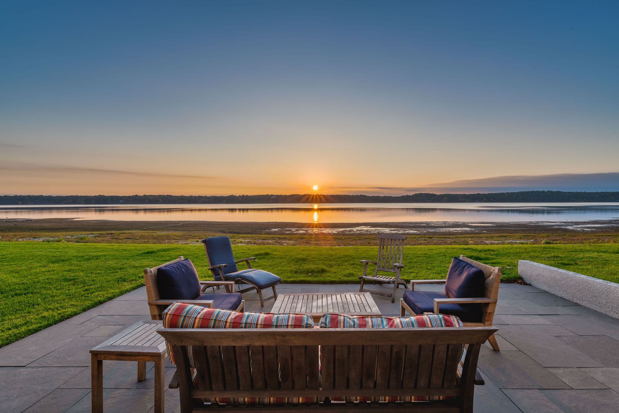 Open patio seating overlooking the lawn and waterfront at sunset.