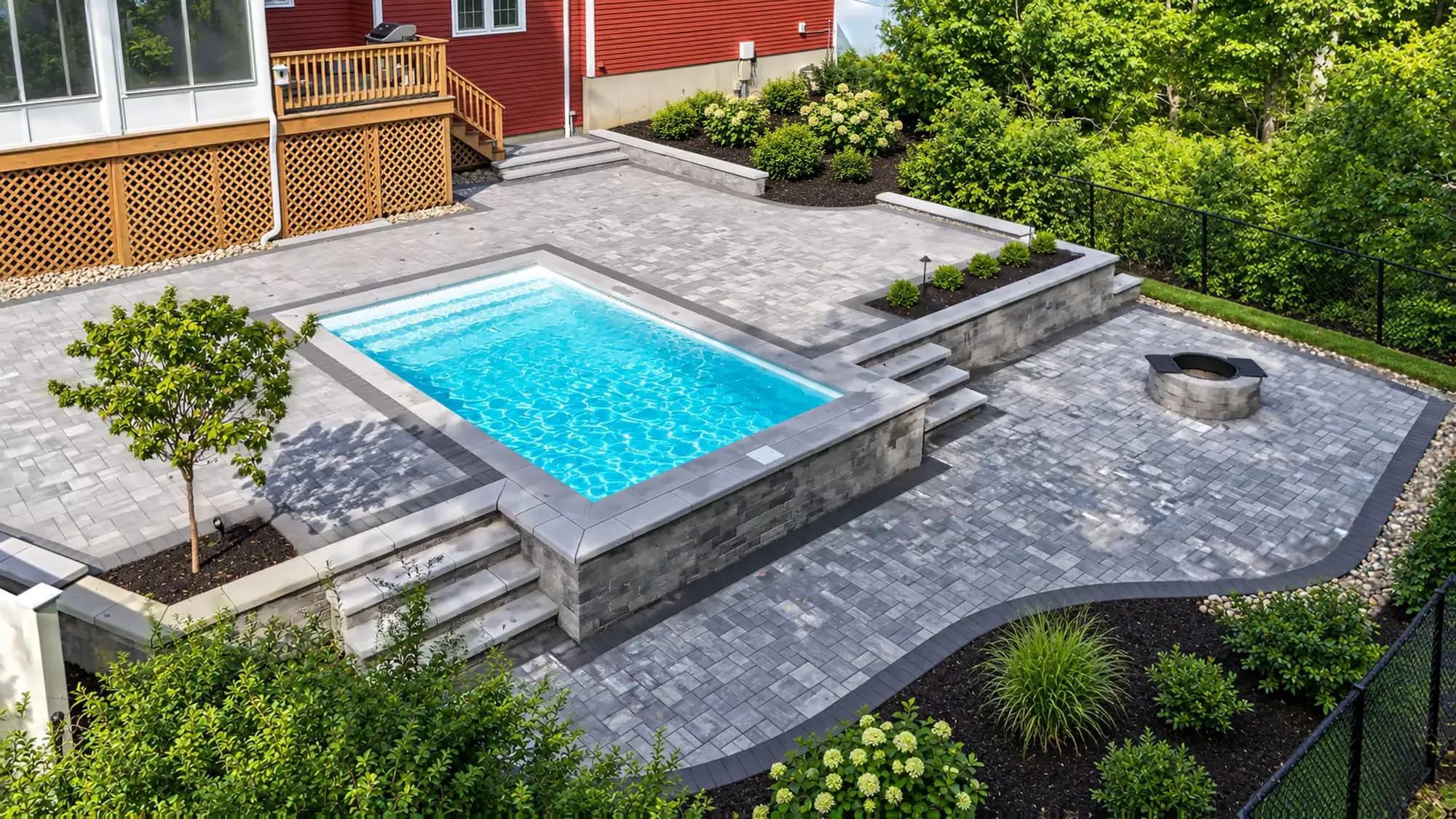 Raised pool with a block retaining wall, steps on both sides, and a lower fire-pit patio in Mansfield, MA.