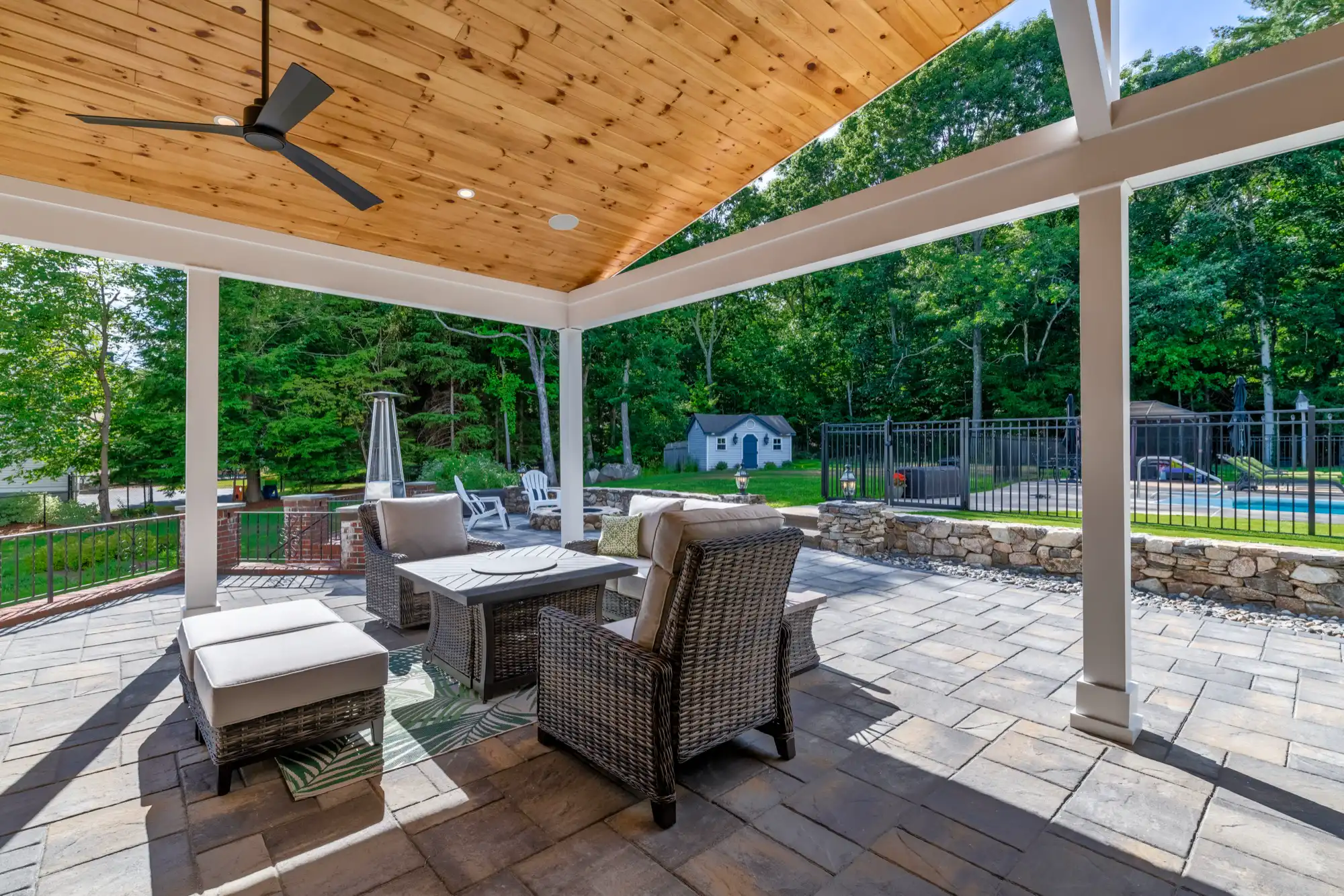 Covered conversation seating beneath the wood ceiling and fan, with the pool beyond.
