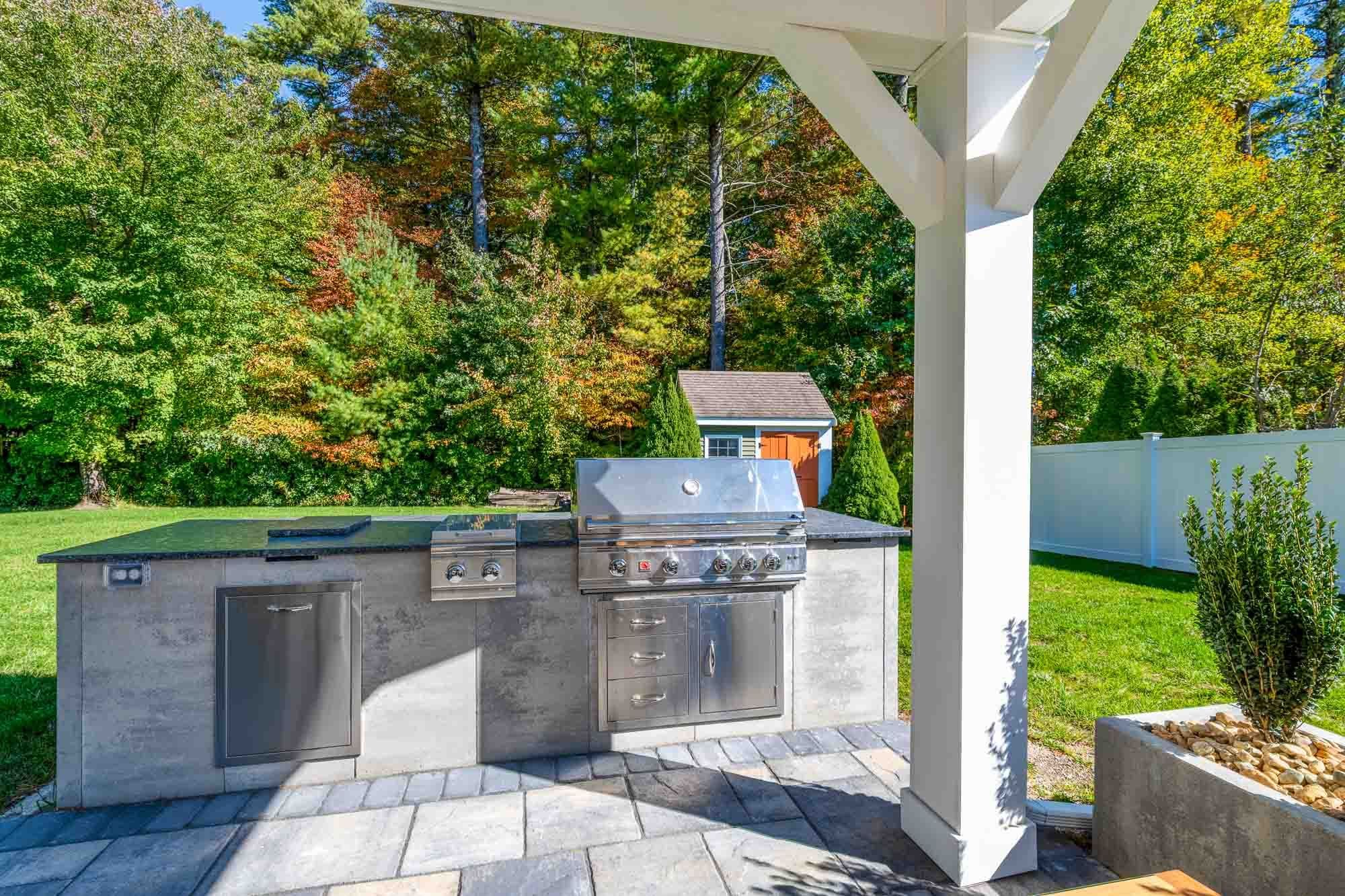 Built-in grill station with storage, a refrigerator, and dark countertops beside the pavilion.