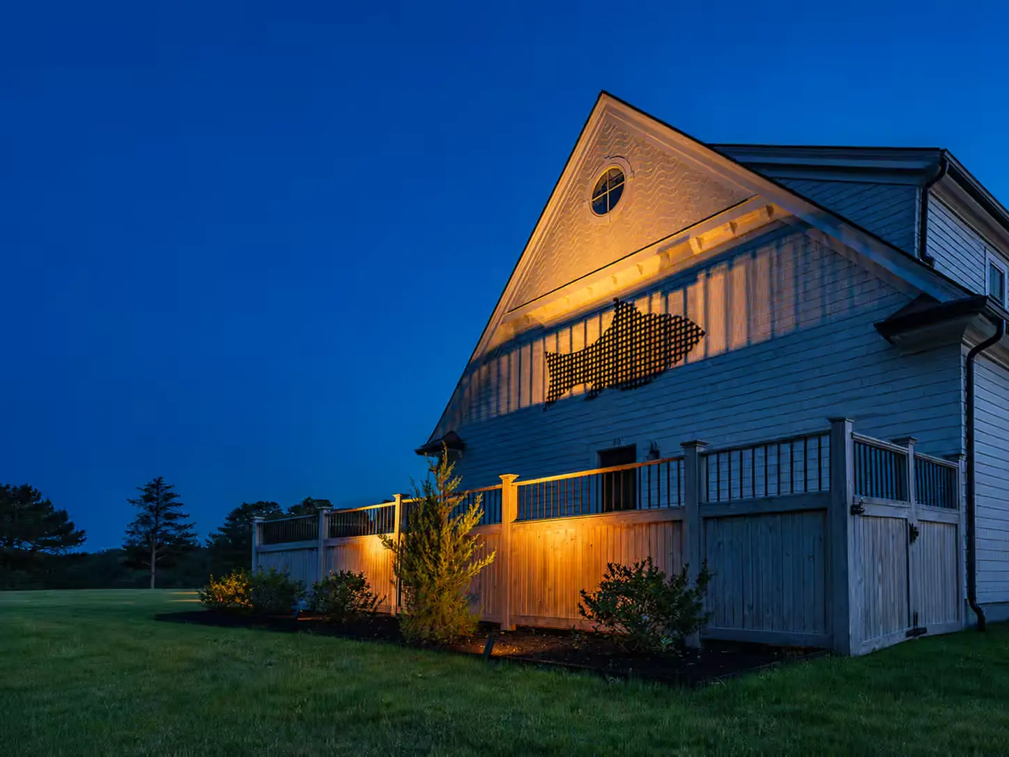 Exterior lighting on the shingled outbuilding at dusk.
