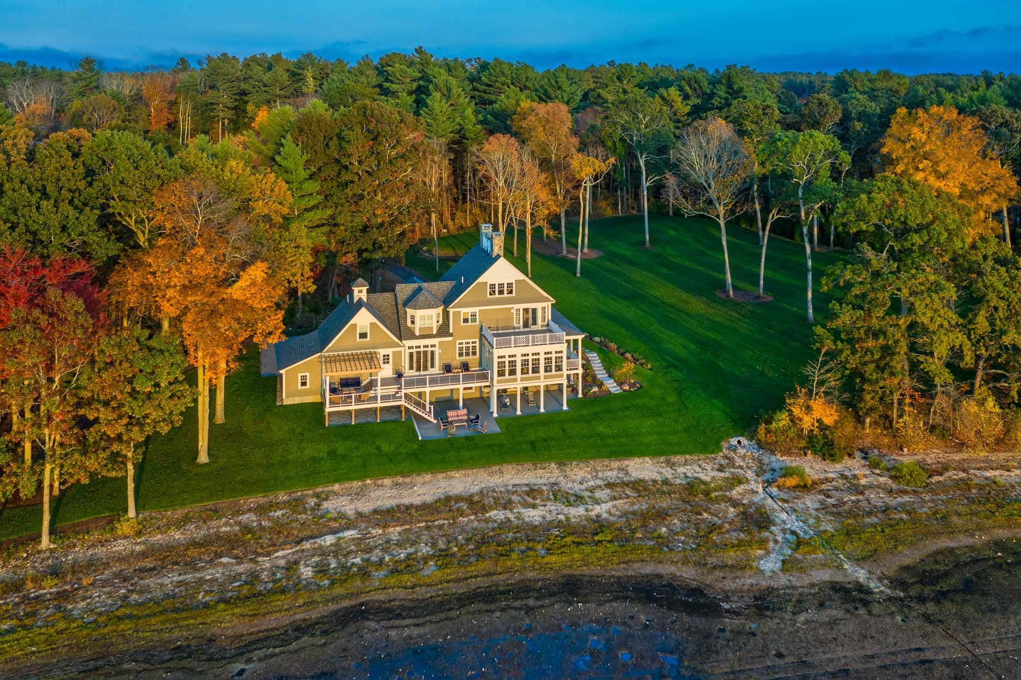 Aerial view of the Pembroke waterfront home, open lawn, and surrounding autumn trees.