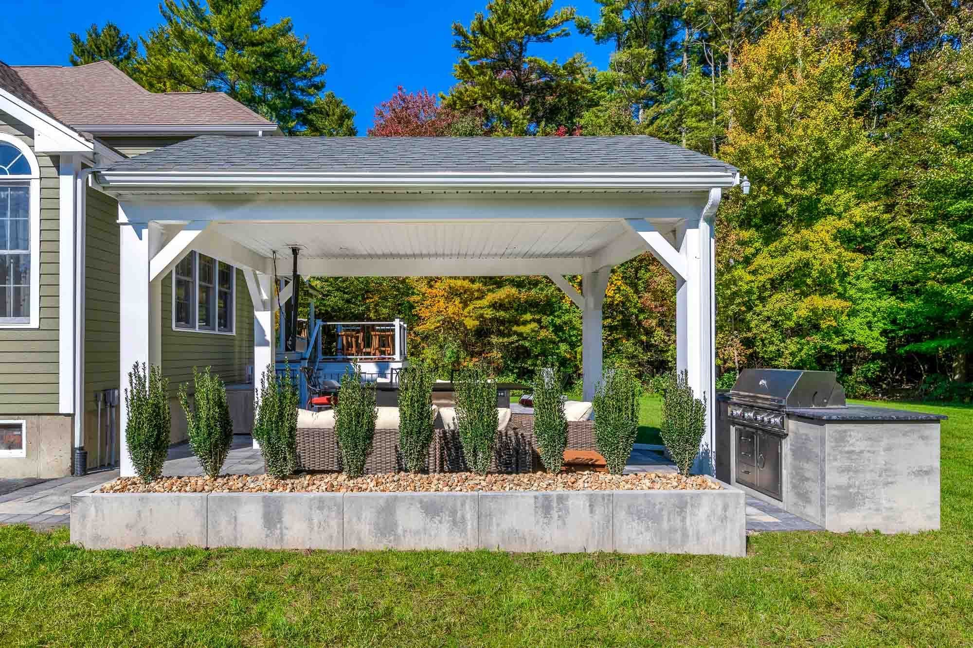 White backyard pavilion framed by raised planting beds, with a grill station beside the lawn.