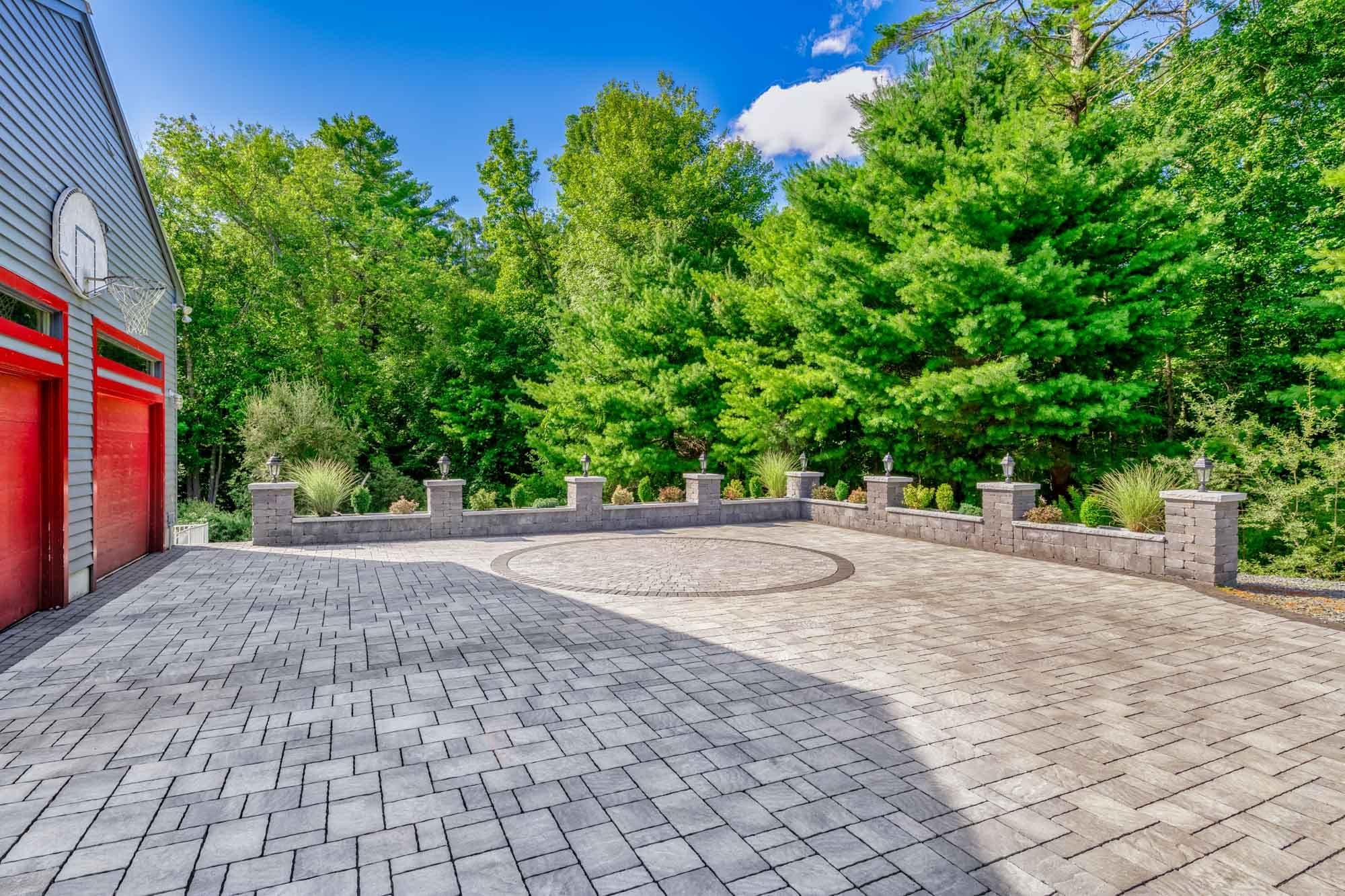 Paver driveway beside the garage, with a circular inlay and lantern-topped perimeter wall.