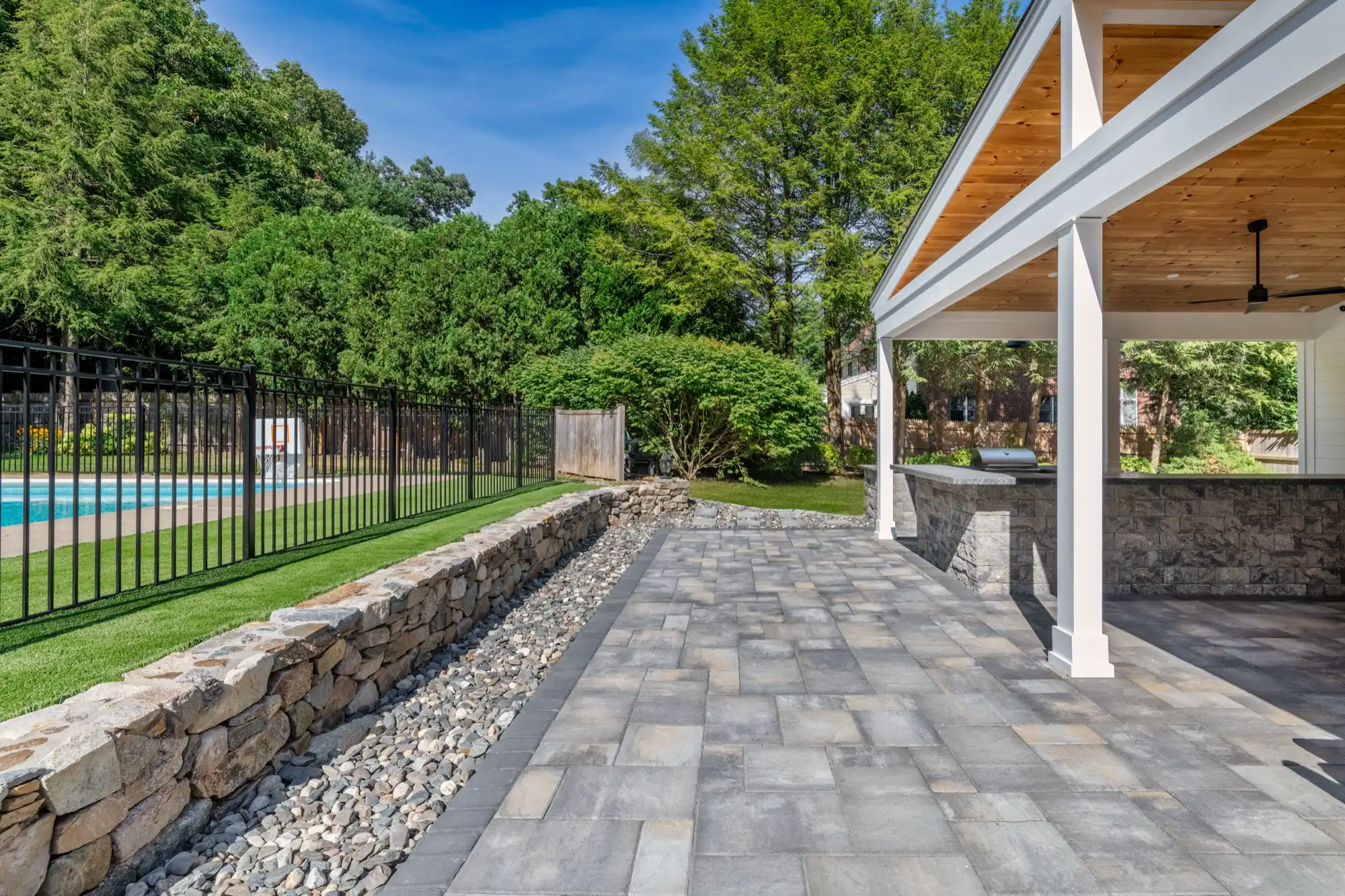 Stone perimeter wall and decorative gravel border along the pavilion patio beside the pool fence.