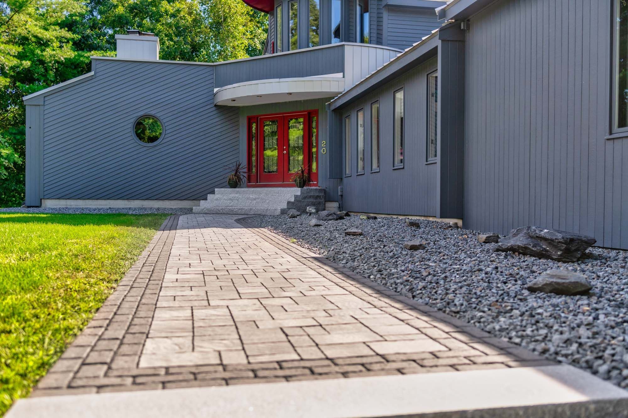 Bordered paver walkway leading toward the red front doors beside a decorative stone bed.