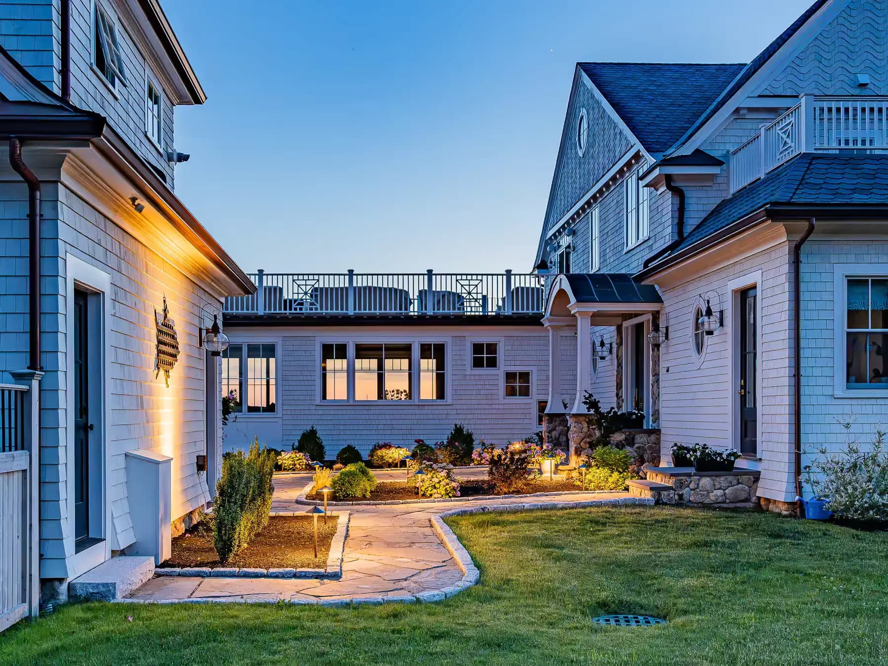 Illuminated paver walkway winding between the buildings and planted beds at dusk.