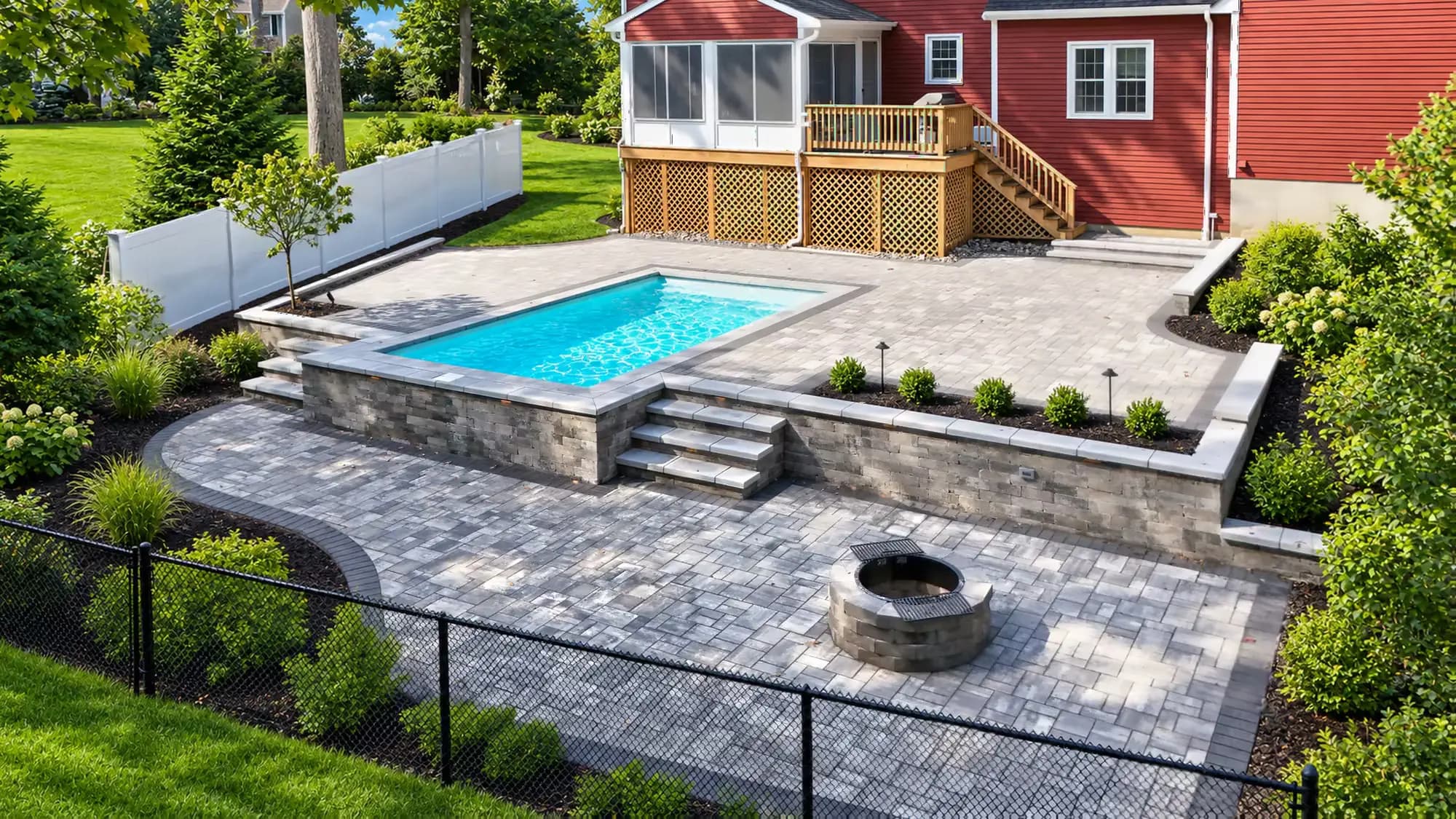 Elevated view of the upper paver patio, raised pool, retaining wall, and fire-pit patio behind the Mansfield home.