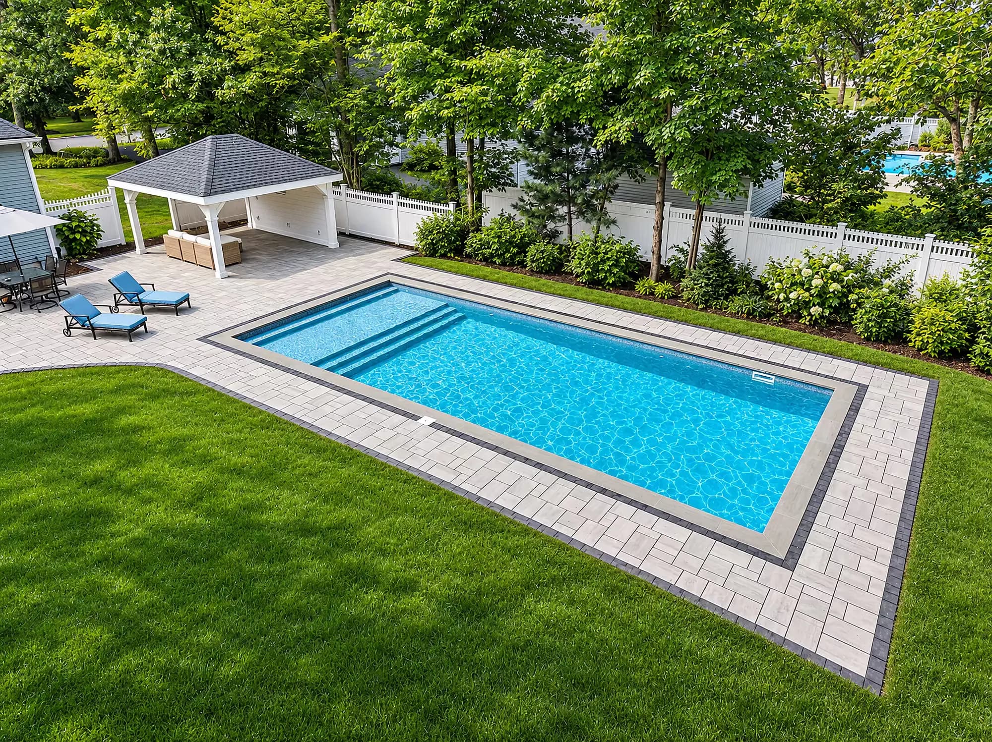 Aerial view of the pool, paver deck, and pavilion beside a fenced planting bed in Mansfield, MA.