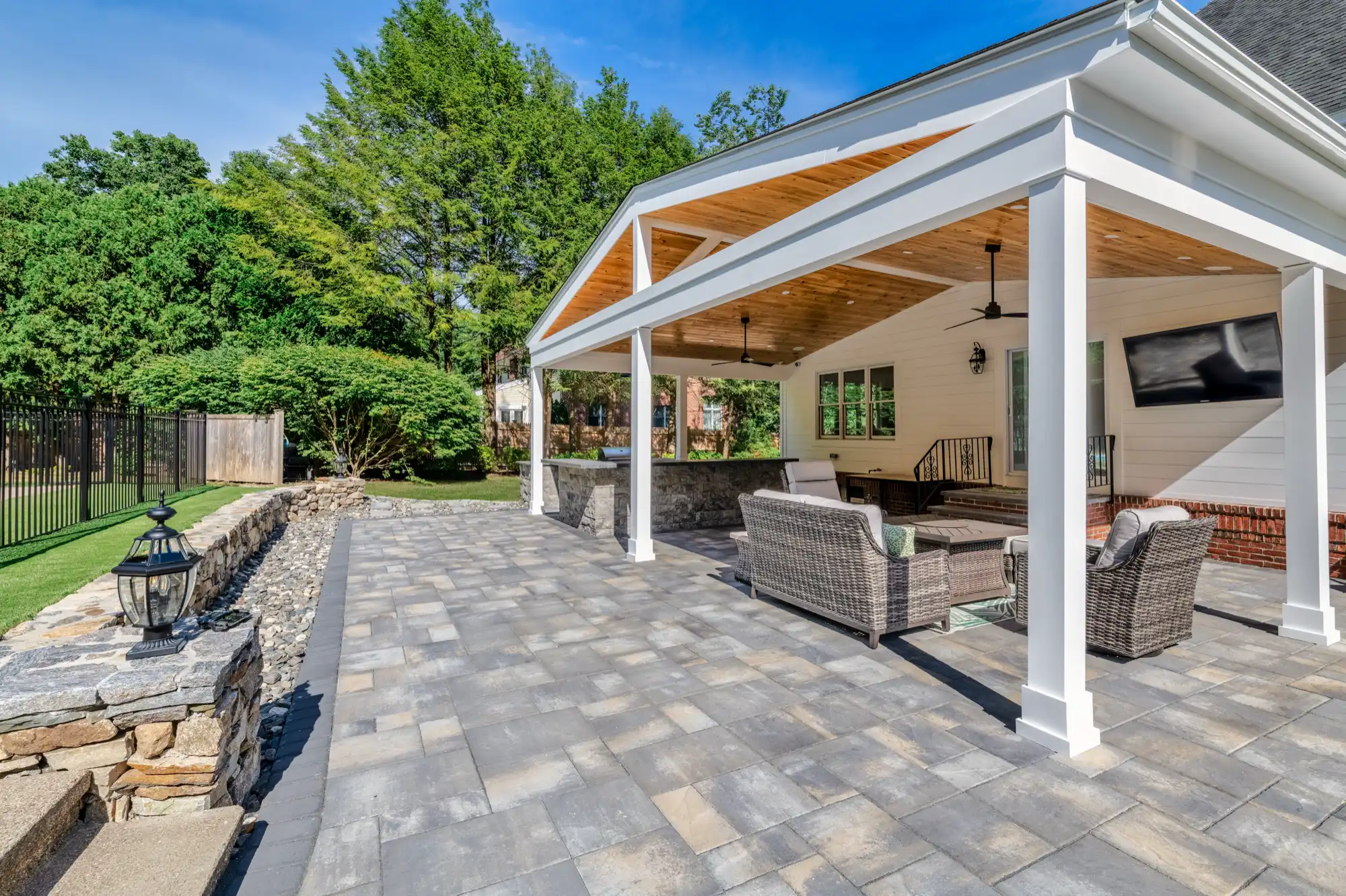 Paver terrace and white pavilion with a wood ceiling, outdoor kitchen, and covered lounge.